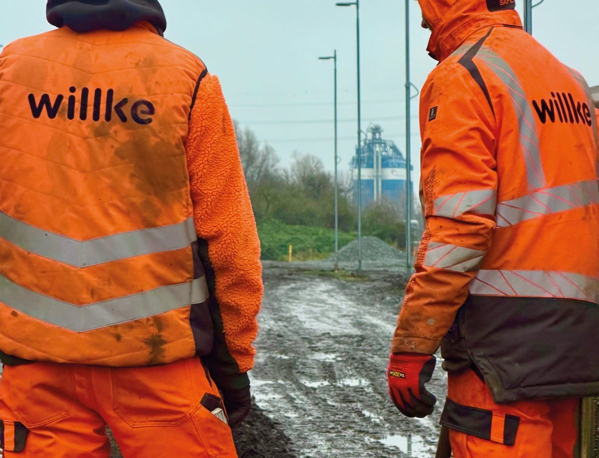 Zwei Gleisbauarbeiter in orangefarbener Arbeitskleidung mit Willke Logo auf dem Rücken.