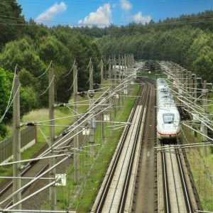 Hochgeschwindigkeitszug fährt auf elektrifizierter Bahnstrecke durch eine grüne Hügellandschaft.
