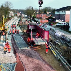 Bahnbaustelle mit zwei Gleisen und mehreren Arbeiter*innen in orangefarbener Warnkleidung.