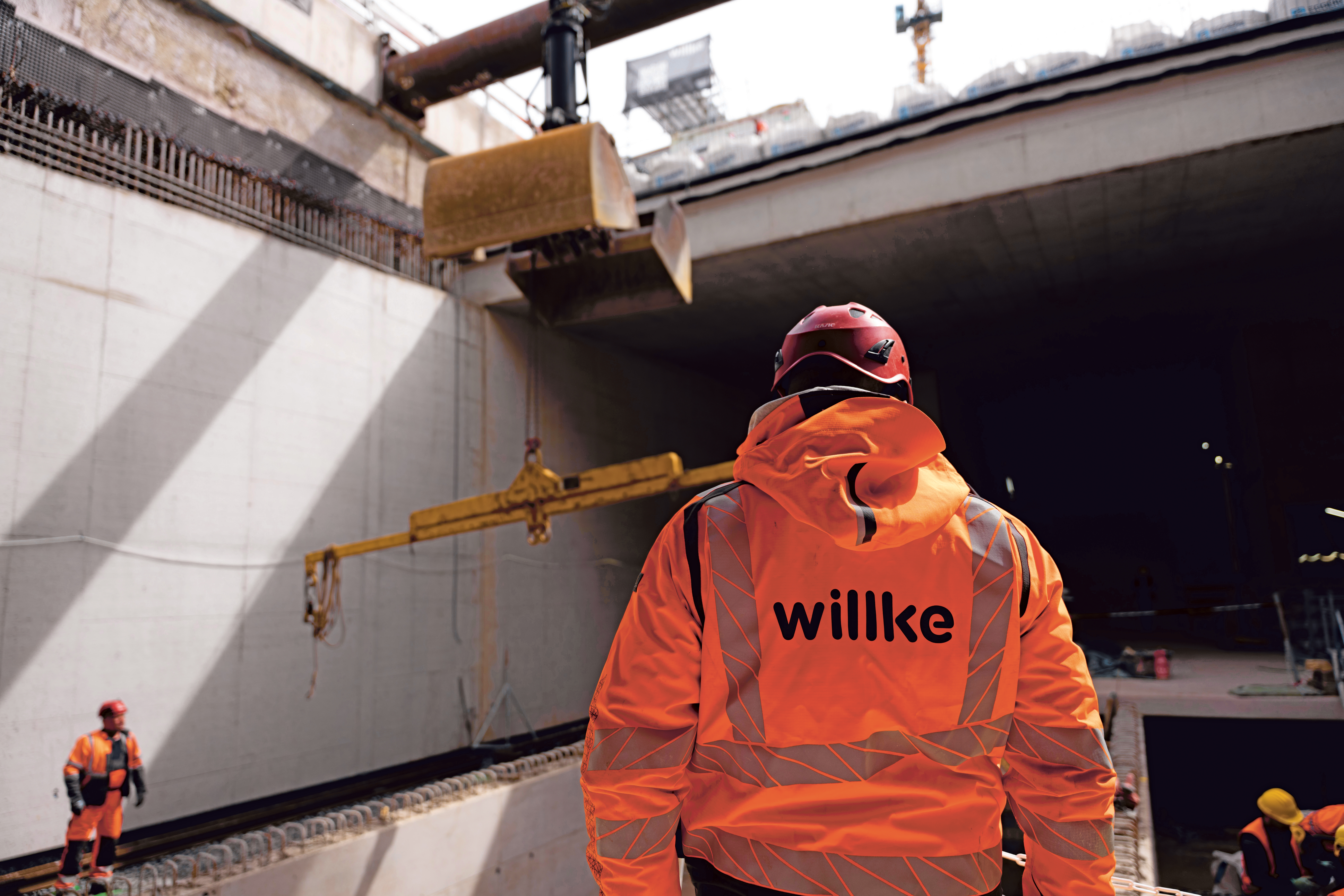 Mitarbeitender in orangener Willke-Kleidung im U5-Bauwerk in Hamburg.