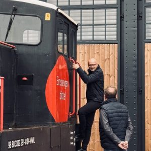 Ein Mann steigt an einer schwarzen Lokomotive die Leiter hoch, während ein anderer unten daneben steht und zuschaut.