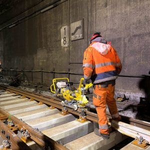 Mitarbeitender arbeitet mit einer Maschine auf einem Gleis im Tunnel.
