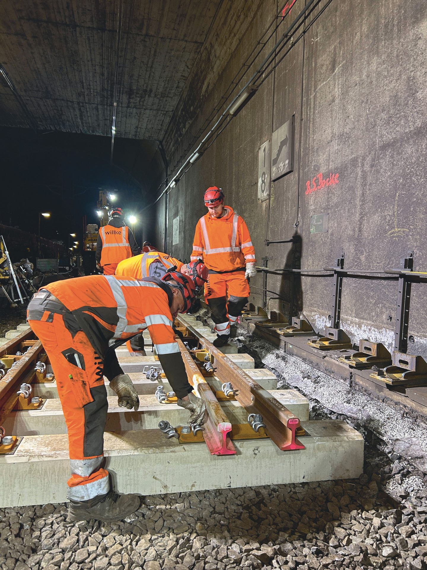 Mehrere Mitarbeitende montieren Gleise auf einer Tunnelbaustelle.