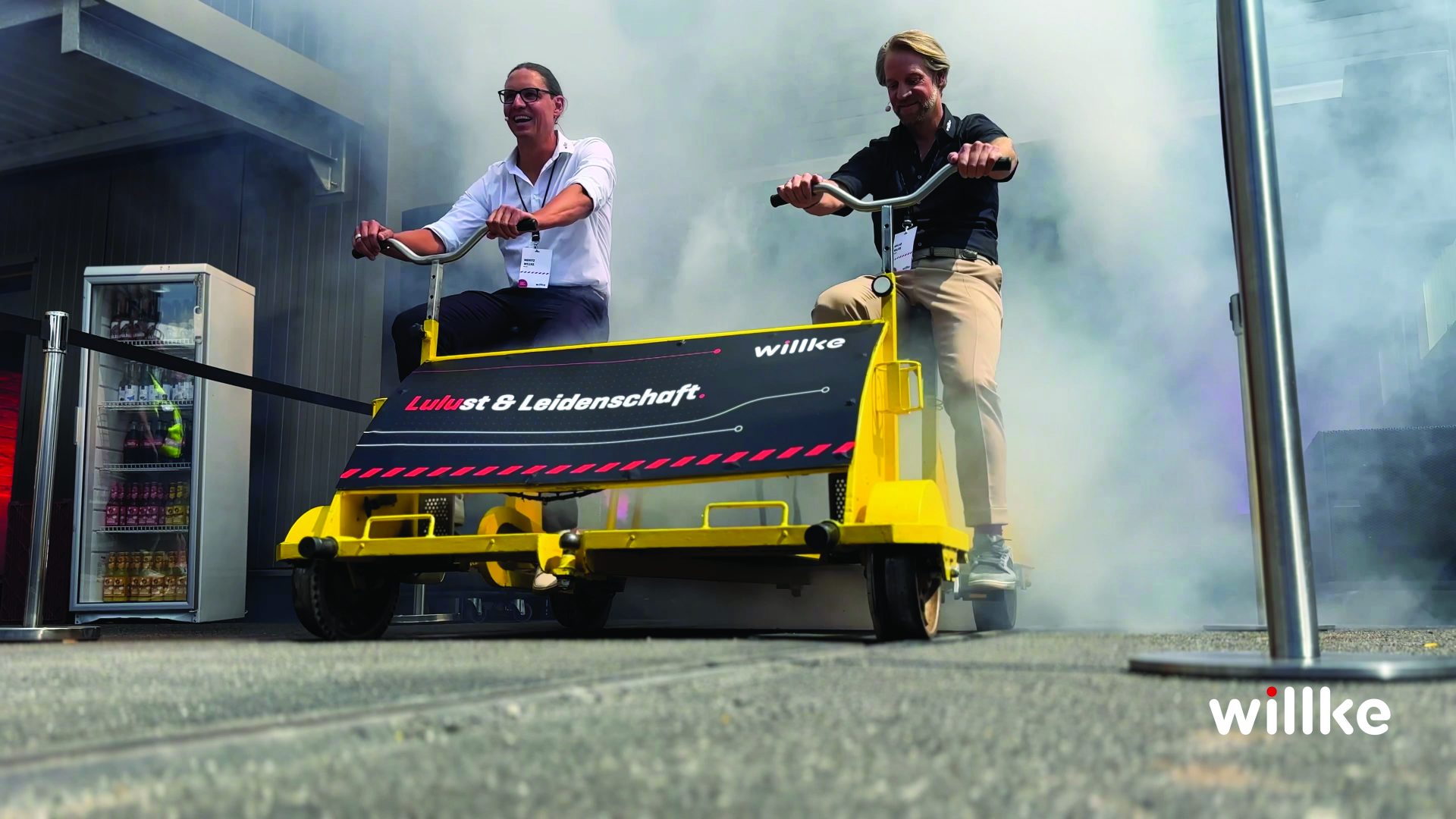 Zwei Männer fahren gemeinsam auf einer gelben Fahrraddraisine im freien umgeben von Nebel.